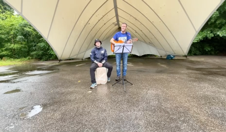 Zwei Männer spielen im Regen ein Lied auf Gitarre und Cajon.